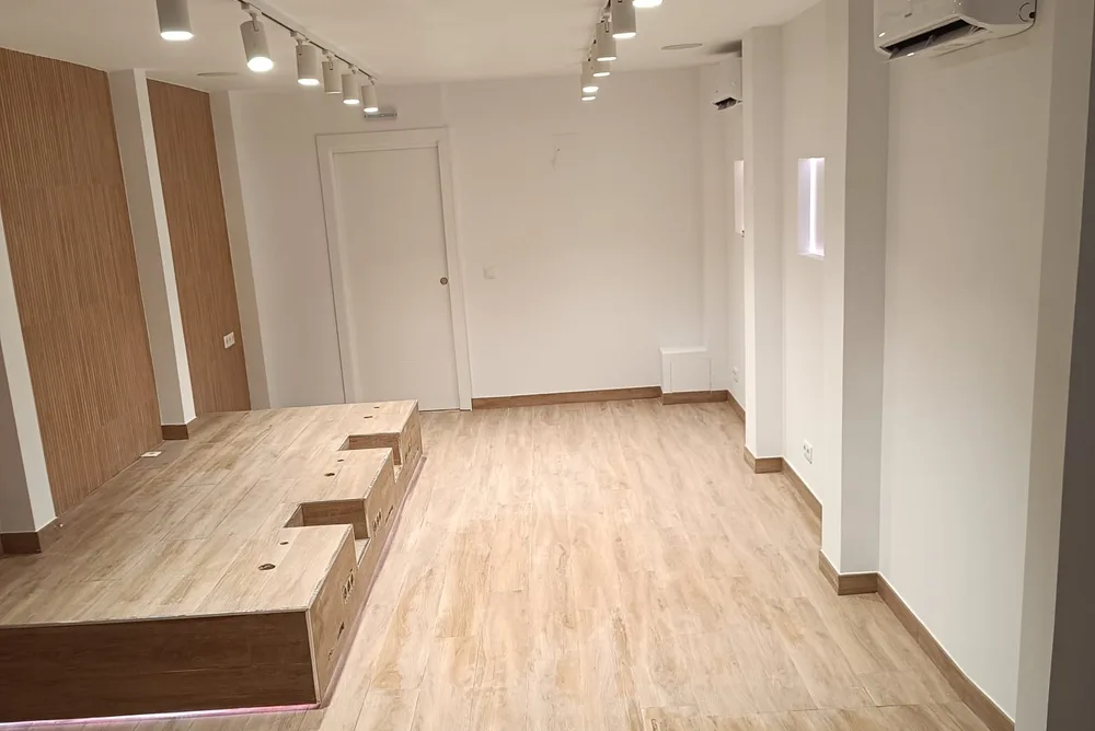 Local comercial reformado con suelo de madera, iluminación en carril y mostrador de obra